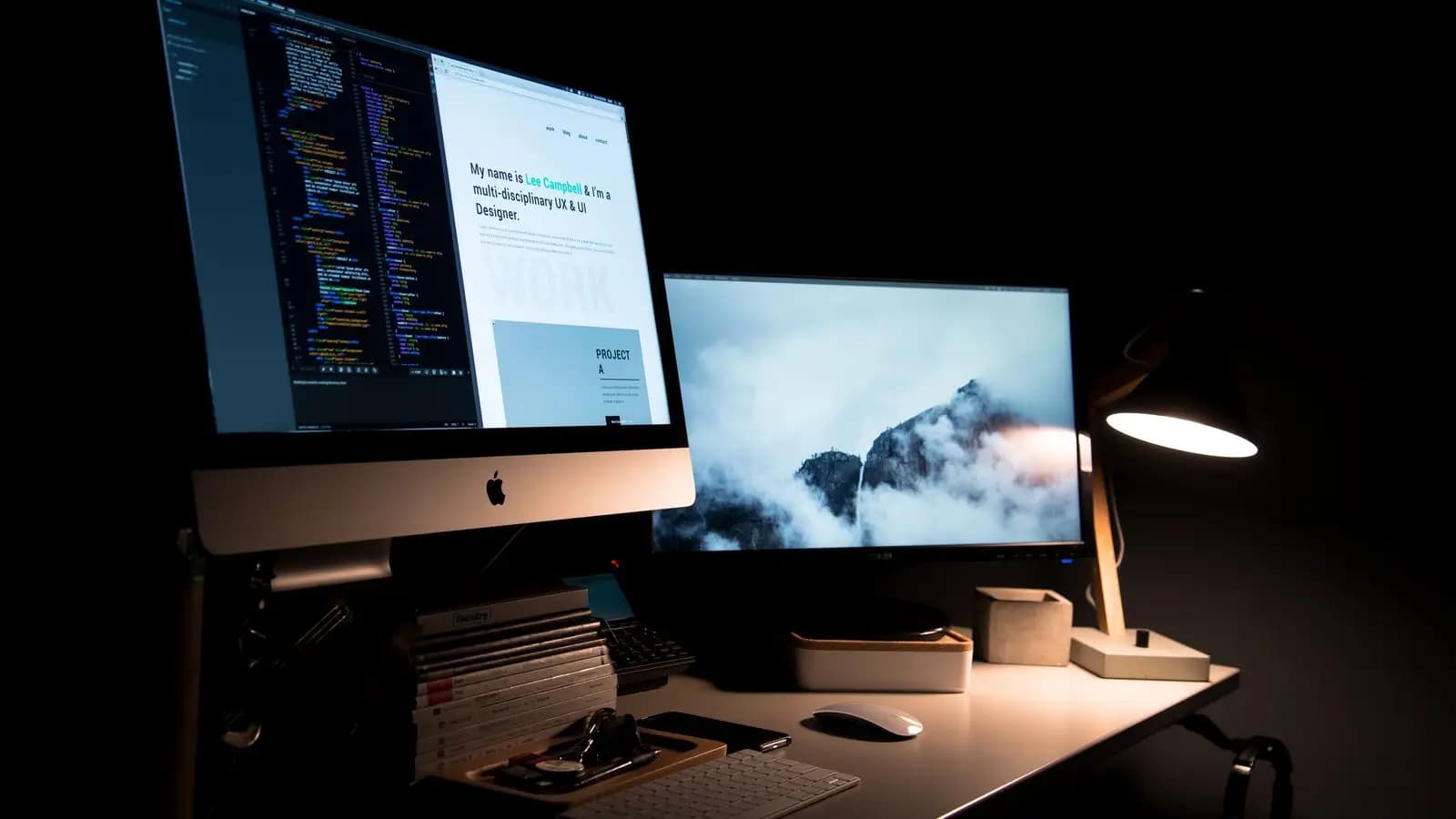 Desk with two monitors and a lamp in a dark room