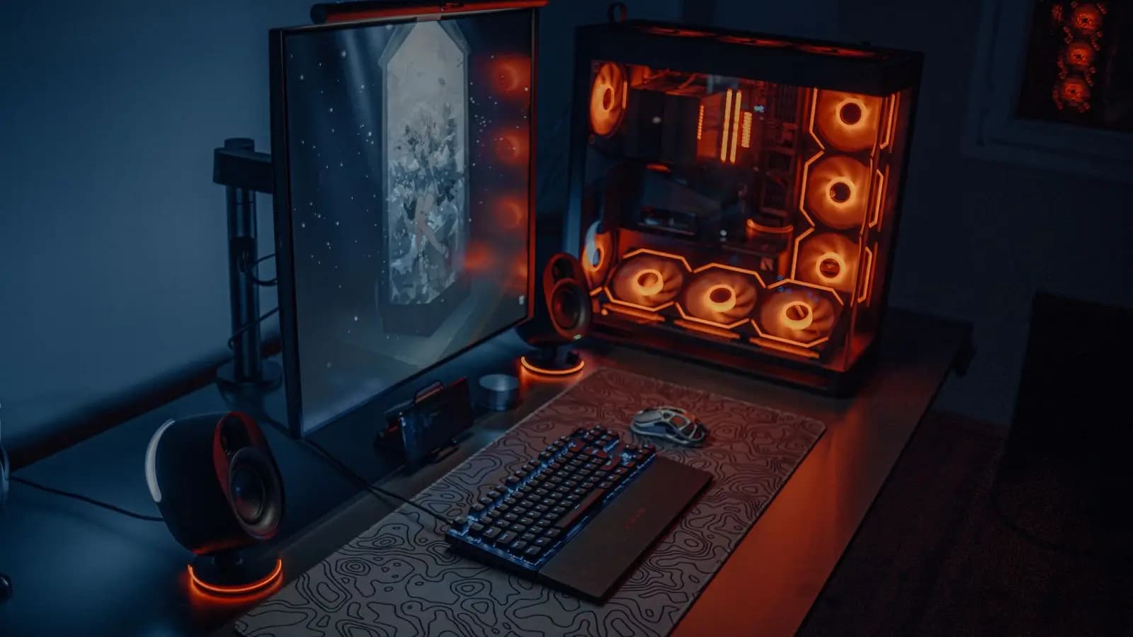 Gaming desk with a large monitor, a keyboard and a PC with glowing fans