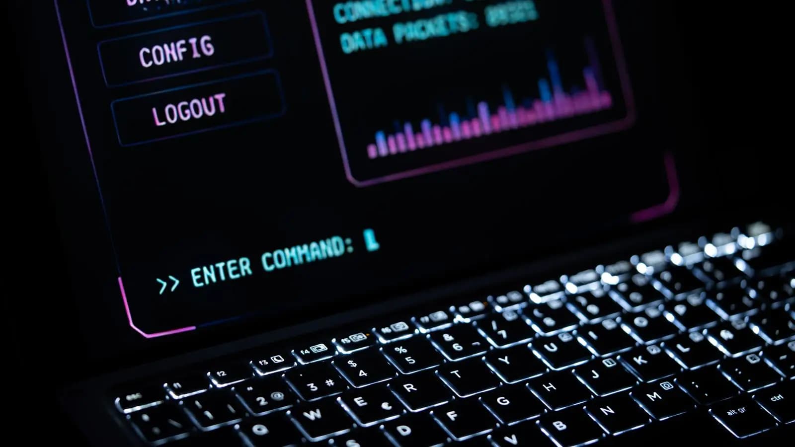 Laptop keyboard lit in the dark under a screen showing a command prompt and a packet graph
